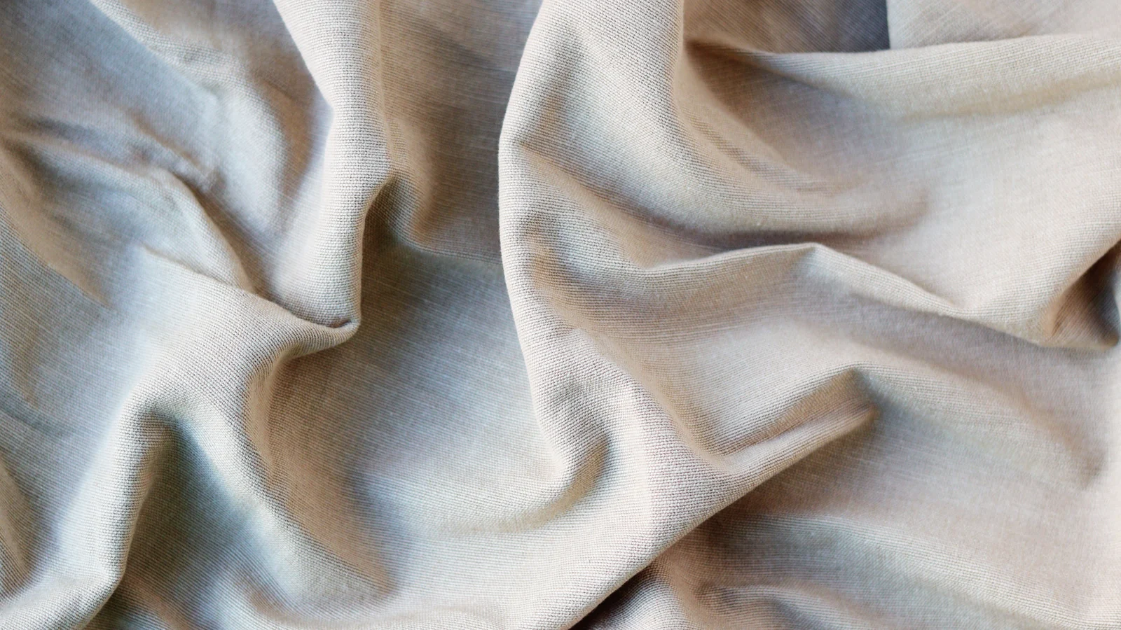 Close-up of beige fabric arranged in loose folds with a visible woven texture.